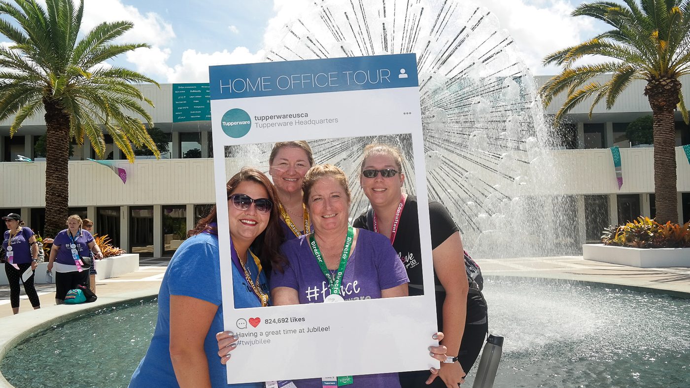 Four guests smiling inside a large photo-frame prop beside a fountain